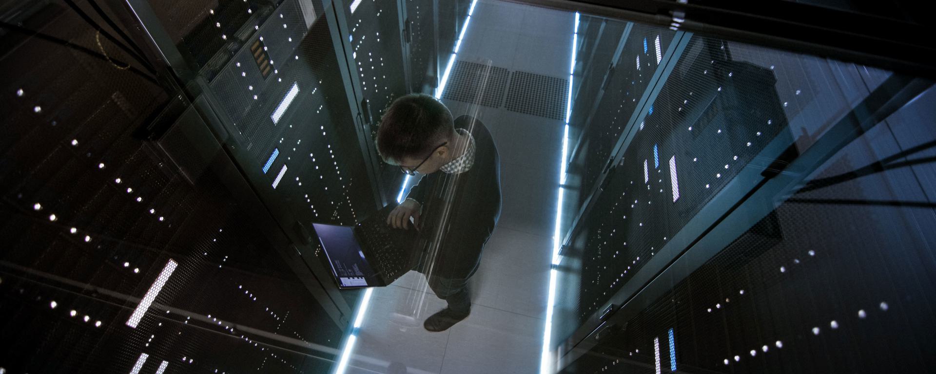 IT engineer working with laptop in data centre full of active rack servers IT engineer working with laptop in data centre full of active rack servers