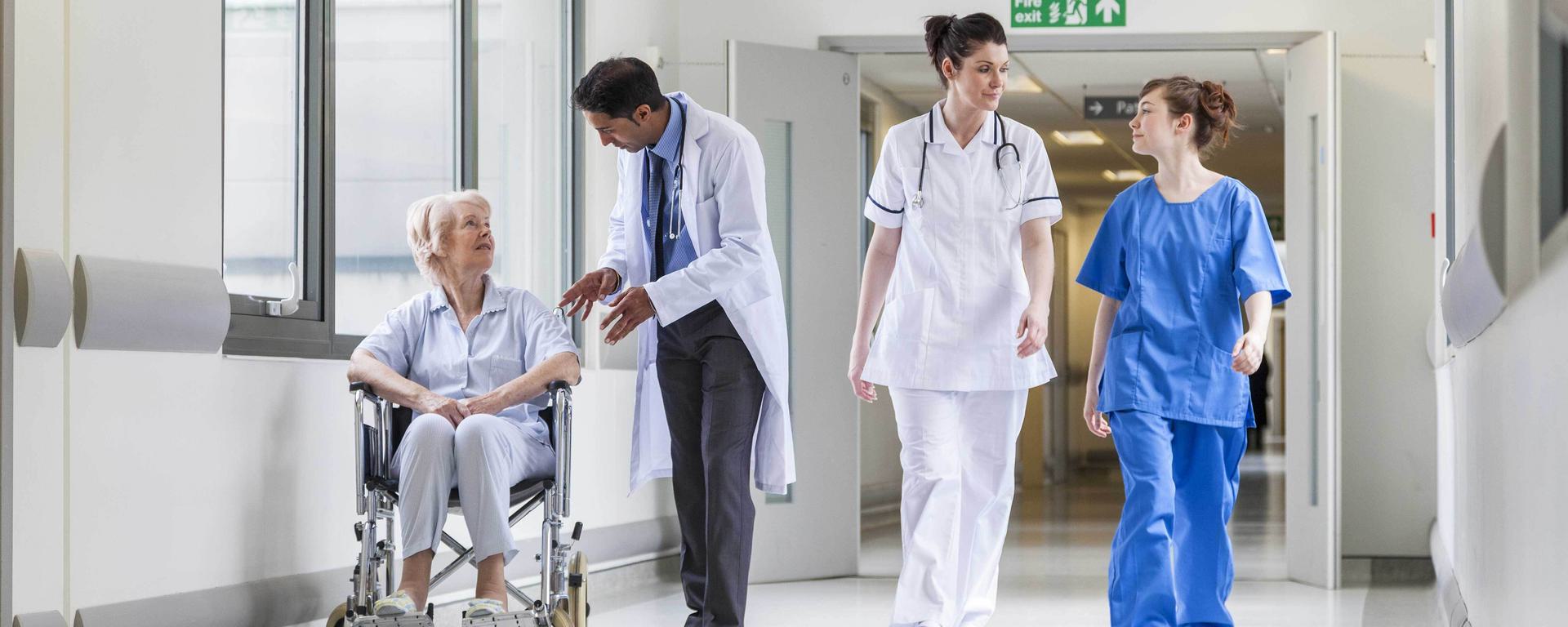 Doctors and nurse with female patient in wheelchair in hospital corridor