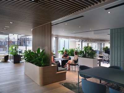 Grainhouse - office floor with planting and people sitting at table in breakout space Grainhouse - office floor with planting and people sitting at table in breakout space