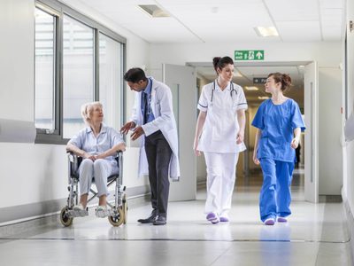 Doctors and nurse with female patient in wheelchair in hospital corridor Doctors and nurse with female patient in wheelchair in hospital corridor