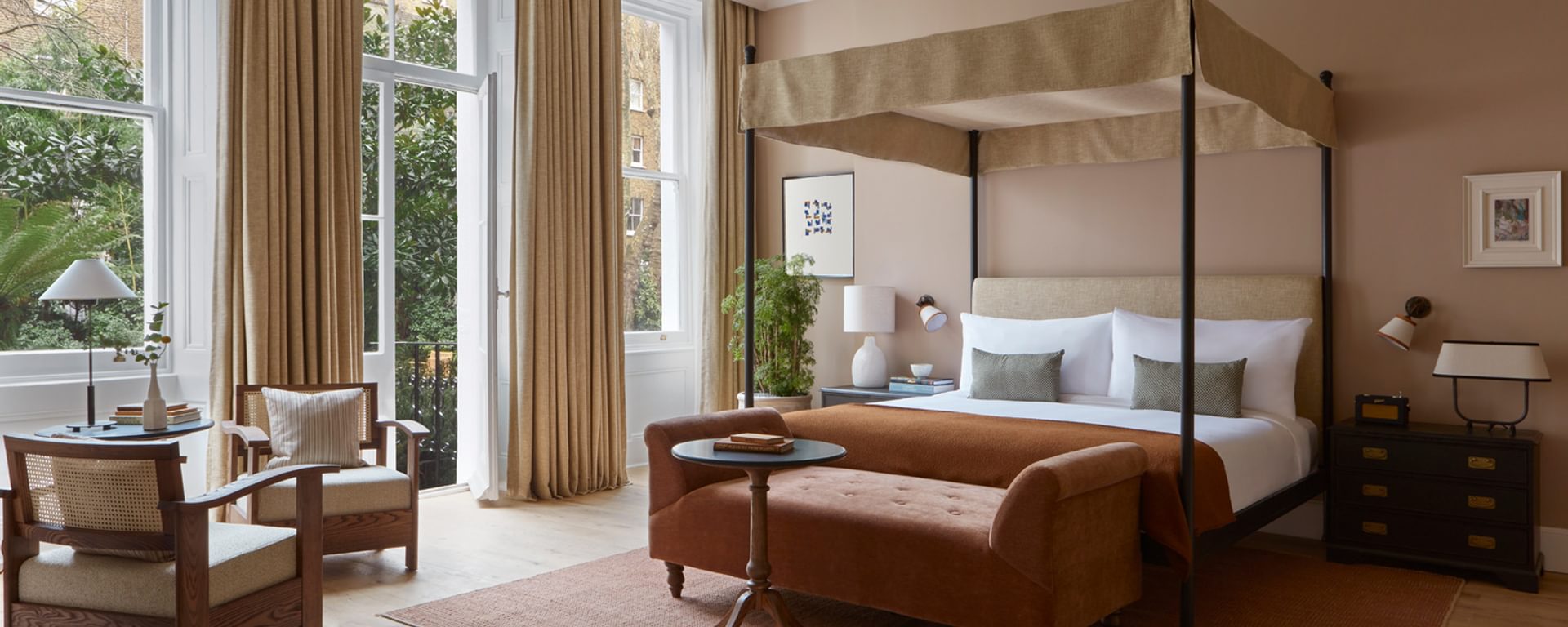 Hotel bedroom with four poster bed, armchair and windows opening out onto garden Hotel bedroom with four poster bed, armchair and windows opening out onto garden