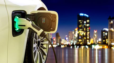 Electric vehicle at charging station with power cable supply plugged in with cityscape in background