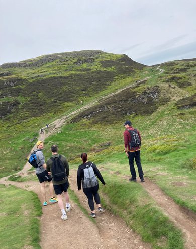A group of people walking down a steep green pathway descending a mountain A group of people walking down a steep green pathway descending a mountain